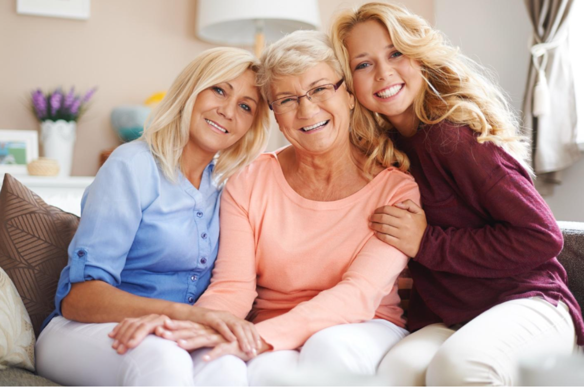 Three generations of women sit on a couch