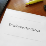 Employee Handbook on a desk with highlighter, clip, and other binders