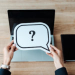 Woman holding a paper with a question mark over a laptop