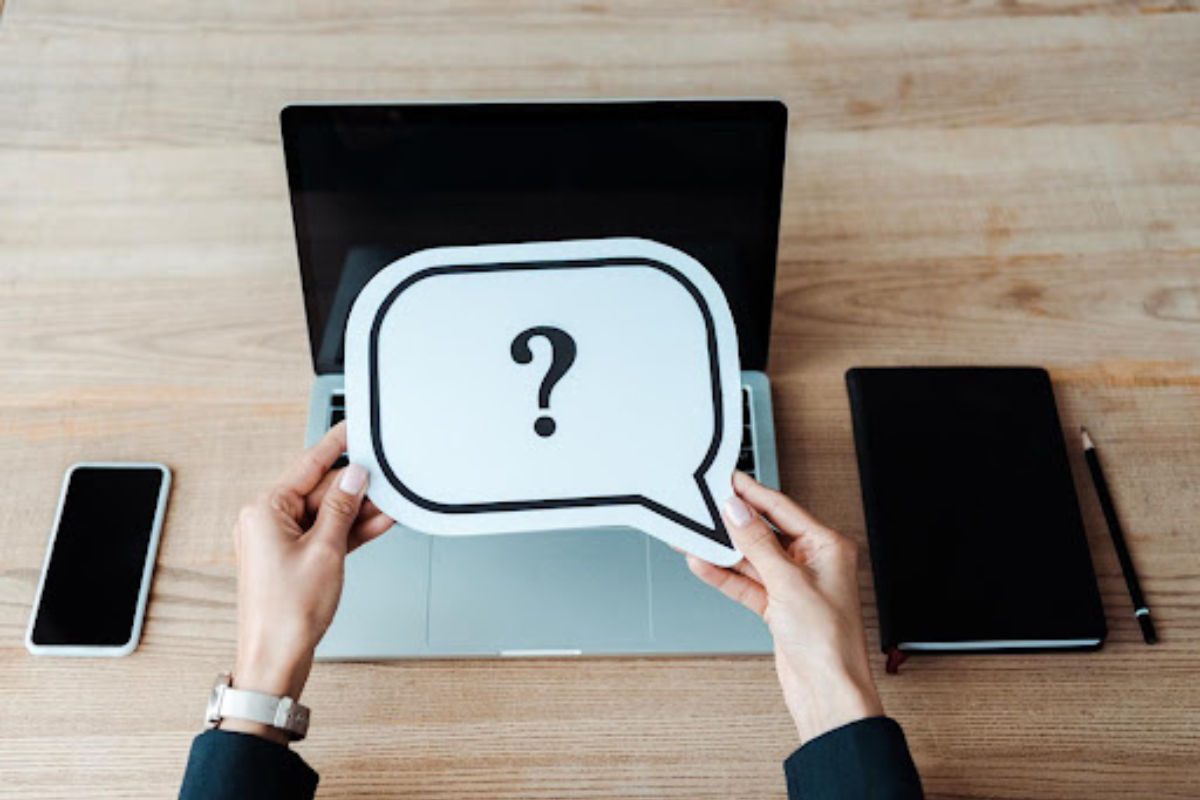 Woman holding a paper with a question mark over a laptop